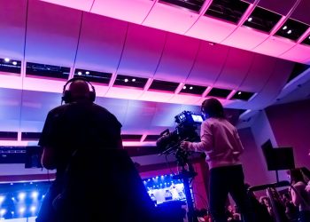 Professional camera crew filming a live event indoors, capturing vibrant stage lighting.