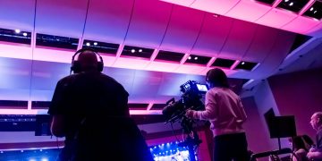Professional camera crew filming a live event indoors, capturing vibrant stage lighting.