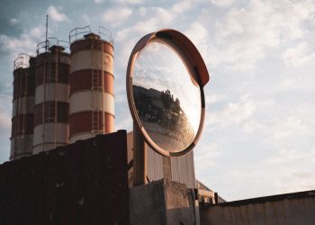 A safety mirror reflects an industrial landscape with silos under a cloudy sky.