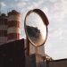 A safety mirror reflects an industrial landscape with silos under a cloudy sky.