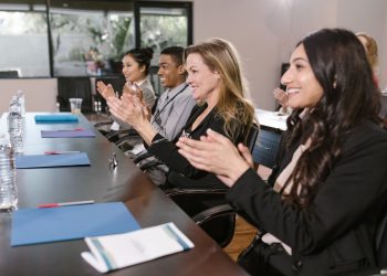 A group of smiling business professionals clapping during a seminar, showcasing success and unity.