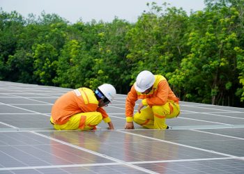 Workers installing photovoltaic solar panels on a sunny day, promoting renewable energy.