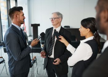 Journalists conduct an interview with a senior executive in a formal office setting.