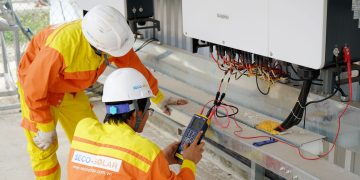 Two electrical engineers installing and testing solar power systems wearing safety gear at a construction site.