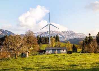 Wind turbine amidst lush country landscape with mountains. A serene depiction of renewable energy in nature.