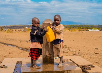 Two children filling a container at a rural water tap on a sunny day.