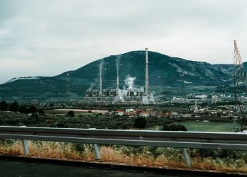 Power plant in a mountainous landscape with smokestacks emitting smoke, highlighting industrial impact on the environment.