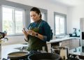 A woman in a modern kitchen following a recipe on her smartphone while cooking.