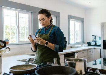 A woman in a modern kitchen following a recipe on her smartphone while cooking.