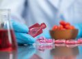 Scientist wearing gloves handling a red liquid vial in a laboratory setting, emphasizing research and medical care.