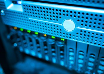 Focused view of a modern data server rack with blinking lights in a blue-lit environment.
