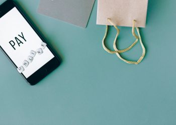 Illustration of online payment with smartphone, credit card, and shopping bag on mint background.