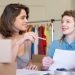 Two businesswomen discussing ideas in an office setting with clothing in the background.