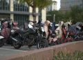 A row of parked scooters and motorcycles in an urban outdoor setting with protective covers.