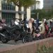 A row of parked scooters and motorcycles in an urban outdoor setting with protective covers.