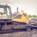 A powerful bulldozer on muddy construction ground under a cloudy sky.