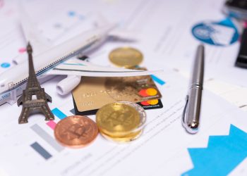 A travel finance concept featuring cryptocurrency, credit card, airplane model, and Eiffel Tower on financial documents.