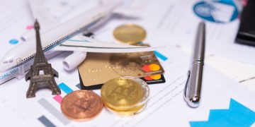 A travel finance concept featuring cryptocurrency, credit card, airplane model, and Eiffel Tower on financial documents.