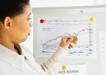 African American woman examines bitcoin and stock market trends on a whiteboard.