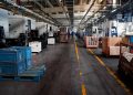 Vast industrial factory floor with machinery, crates, and structured workstations.