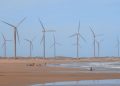 Scenic wind turbines at Icaraí beach, Ceará, Brazil with surfers nearby.