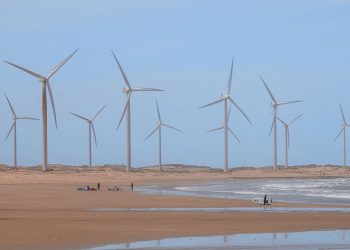 Scenic wind turbines at Icaraí beach, Ceará, Brazil with surfers nearby.