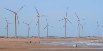 Scenic wind turbines at Icaraí beach, Ceará, Brazil with surfers nearby.