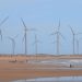 Scenic wind turbines at Icaraí beach, Ceará, Brazil with surfers nearby.