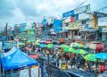 A bustling market with colorful umbrellas and billboards in Lagos, Nigeria.