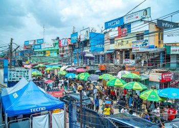 A bustling market with colorful umbrellas and billboards in Lagos, Nigeria.