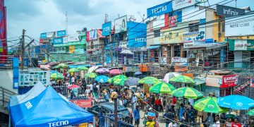 A bustling market with colorful umbrellas and billboards in Lagos, Nigeria.