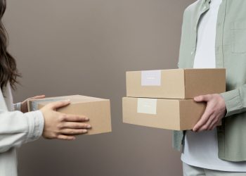 Two people exchanging cardboard boxes indoors, emphasizing teamwork and logistics.