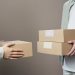 Two people exchanging cardboard boxes indoors, emphasizing teamwork and logistics.