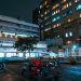 Night view of a hospital with scooters parked outside, illuminated by bright city lights.