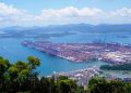 Aerial image of a bustling industrial port with containers in a scenic coastal setting.