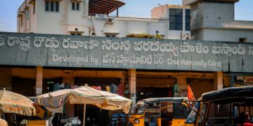 A vibrant urban street market scene with auto rickshaws and local shops.