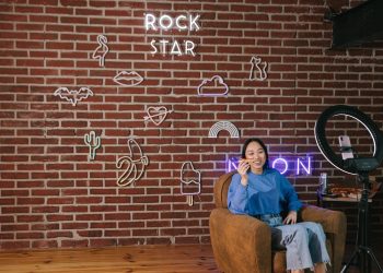 Asian woman streaming content with neon signs on a brick wall. Modern influencer setup.