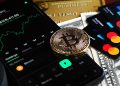 Bitcoin coin with financial data, credit cards, and currency on a desk.
