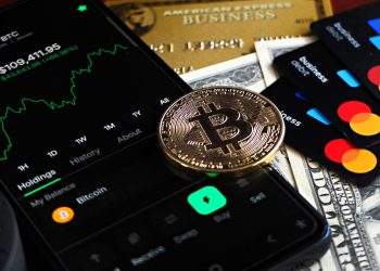Bitcoin coin with financial data, credit cards, and currency on a desk.