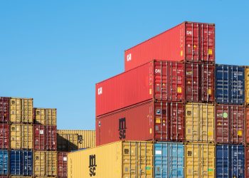 A vibrant collection of stacked shipping containers under a clear, blue sky. Ideal for logistic themes.