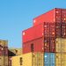 A vibrant collection of stacked shipping containers under a clear, blue sky. Ideal for logistic themes.