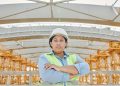 Female engineer in safety gear at a construction site with steel structure background.