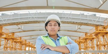 Female engineer in safety gear at a construction site with steel structure background.