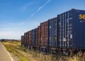 Colorful cargo containers on a freight train along a rural railway track under a clear blue sky.