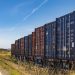 Colorful cargo containers on a freight train along a rural railway track under a clear blue sky.