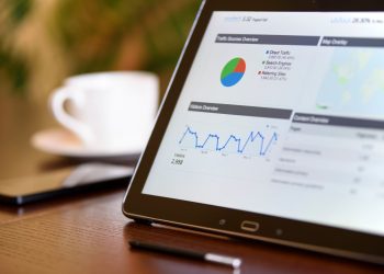 Close-up of a tablet displaying analytics charts on a wooden office desk, alongside a smartphone and coffee cup.