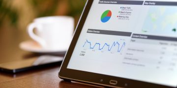 Close-up of a tablet displaying analytics charts on a wooden office desk, alongside a smartphone and coffee cup.