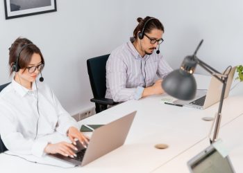 Two office workers focusing on tasks at a call center, using laptops and headsets.