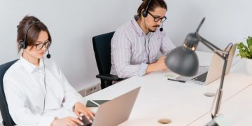 Two office workers focusing on tasks at a call center, using laptops and headsets.