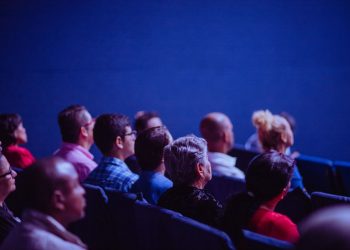 An attentive group of adults seated at an indoor conference, focusing on a presentation.